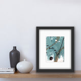 An abstract acrylic painting in a white mat,and framed in a modern black frame. The colours are teal, burnt umber and white. The painting is sitting on a shelf beside two vases and some books.