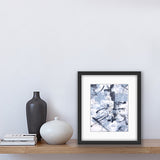 An abstract acrylic painting on paper in a black frame. The colours are a soft grey/blue, black and white. The painting sits on a shelf beside two vases and some books.